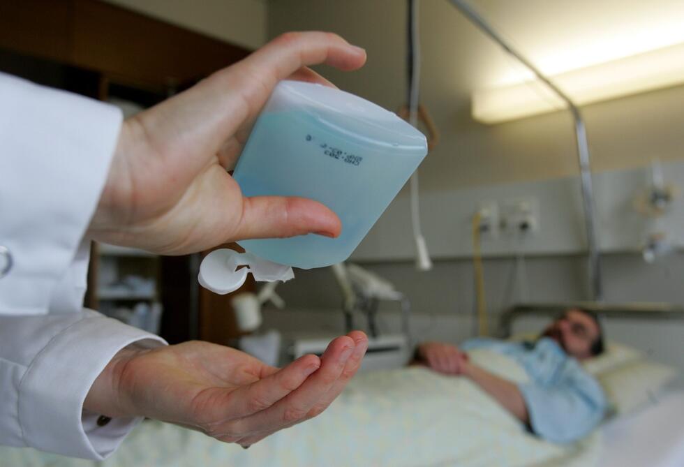 Someone disinfecting his hands next to the hospital bed with a patient in it