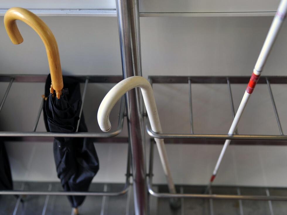 An umbrella, a walking aid and a blind stick in a tray